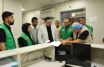 Group of aid workers in green vests gather around a reception desk as a man signs papers.