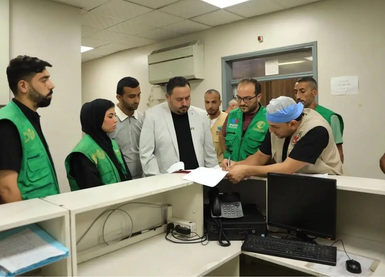 Group of aid workers in green vests gather around a reception desk as a man signs papers.