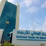 Facade of the National Center for Meteorology with a blue glass tower and a large sign in Arabic and English in front of the building.