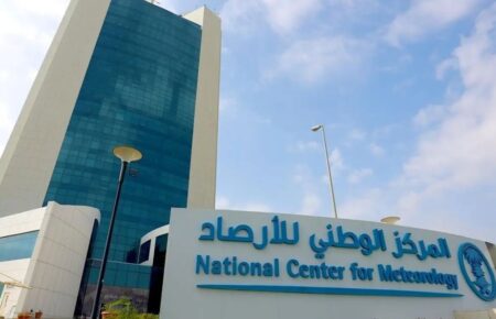 Facade of the National Center for Meteorology with a blue glass tower and a large sign in Arabic and English in front of the building.