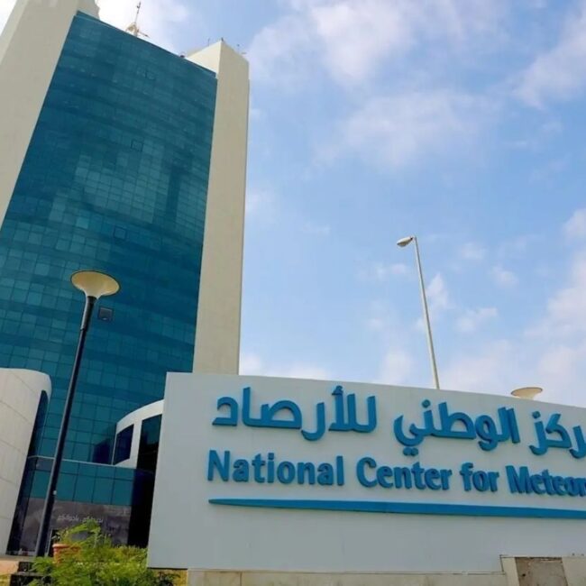 Facade of the National Center for Meteorology with a blue glass tower and a large sign in Arabic and English in front of the building.