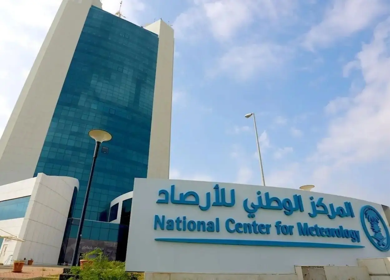 Facade of the National Center for Meteorology with a blue glass tower and a large sign in Arabic and English in front of the building.
