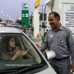 Gas station attendant chats with a driver inside a car at the fueling pump.