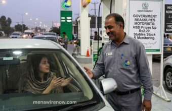 Gas station attendant chats with a driver inside a car at the fueling pump.