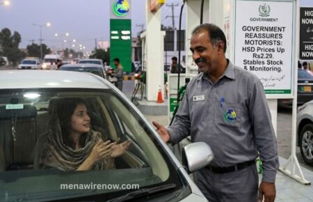 Gas station attendant chats with a driver inside a car at the fueling pump.
